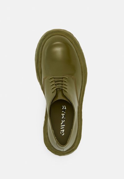 Zapatos de cordones de color verde olivo con parte superior de cuero suave, puntera redonda y suela de goma gruesa con costuras visibles y marca en el interior.