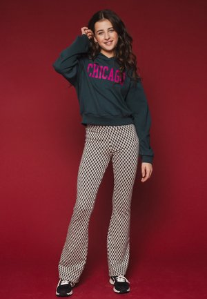 Dark green hoodie with pink "CHICAGO" text, paired with black and white patterned flared pants. Black sneakers complete the outfit.