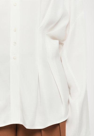 White blouse with a smooth, flowing texture, featuring a button-down front and slight pleats at the sides for added shape and detail.