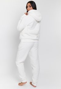 Ensemble de vêtements de détente en polaire blanche comprenant une veste à capuche zippée et un pantalon fuselé avec des poignets côtelés. Tissu doux et texturé avec poches.