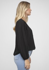 Top negro de manga larga con un ajuste relajado y puños elásticos, confeccionado con tela ligera, combinado con vaqueros azul claro.