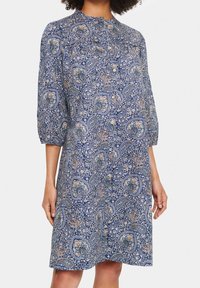 Blå paisleyklänning med 3/4 ärmar, knapprad fram och avslappnad passform. Tyget har intrikata blommönster med beige och gröna accenter.