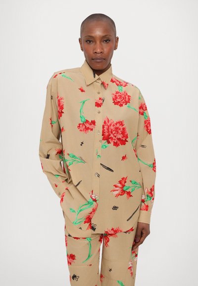 Camisa beige de botones con grandes patrones florales rojos y hojas verdes. Corte holgado con mangas largas, combinada con pantalones florales a juego.