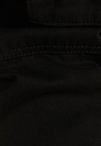 Mustaa kangasta, jossa on sileä pinta ja ommeltu sauma. Pinta näyttää pieniä vaihteluita, mikä osoittaa materiaalin joustavuutta.