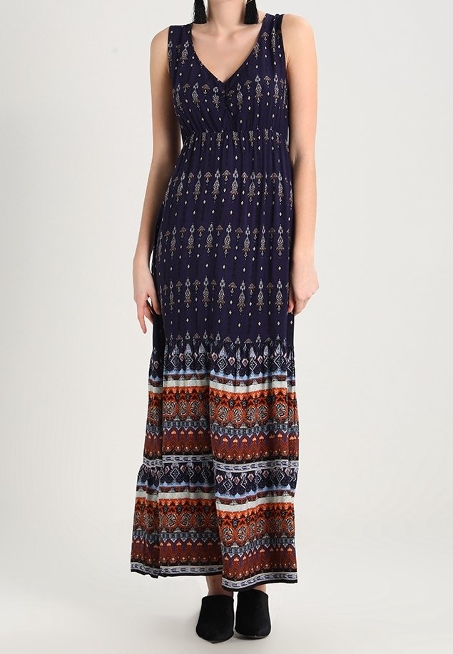 Mouwloze marineblauwe maxi-jurk met V-hals, bedekt met beige en meerkleurige geometrische patronen, gedragen met zwarte instap schoenen.