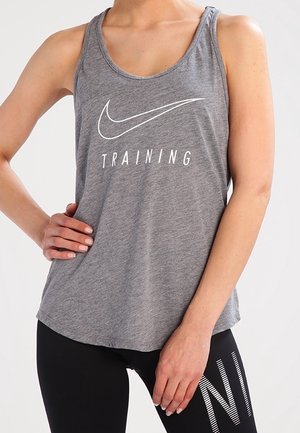 Personne portant un débardeur d'entraînement gris avec un logo Nike blanc et un legging noir avec un texte blanc sur une jambe.