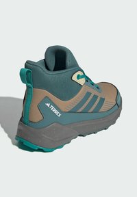 Brown and teal hiking shoe with mesh upper, padded collar, and prominent tread. Features logo and three stripes detailing.