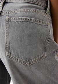 Gray denim jeans with a back pocket. Features light stitching and a slightly faded texture, adding subtle design detail.