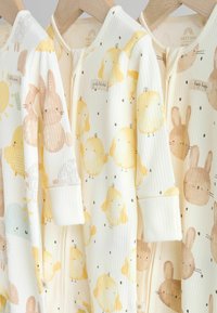 Tre babybodys i mjukt ribbat tyg med pastellfärger. Designen inkluderar gula kycklingar och bruna kaniner med små prickar.