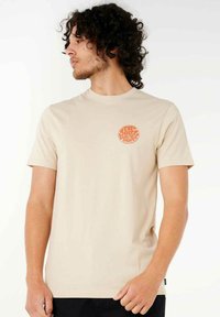 Beige bomulds t-shirt med et rundt orange logo-design på venstre bryst. Korte ærmer og rund hals fuldender det enkle look.