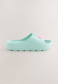 Sandale slip-on bleu sarcelle clair avec un avant ouvert, une semelle épaisse et un charm rose décoratif sur le dessus sur fond uni.