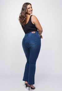 Donkerblauwe jeans met een uitlopende snit, hoge taille en zichtbare achterzakken. De stof is denim met een zachte textuur en een lichte stretch.