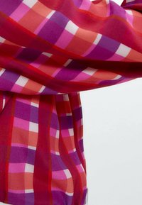Blusa trasparente a maniche lunghe in un vivace motivo scozzese rosso, rosa e viola. Tessuto leggero con una texture liscia e una vestibilità comoda.