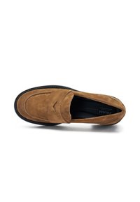 Mocassino in suede marrone con punta arrotondata, dettagli di cucitura discreti e suola in gomma nera. L'interno è foderato in tessuto nero.
