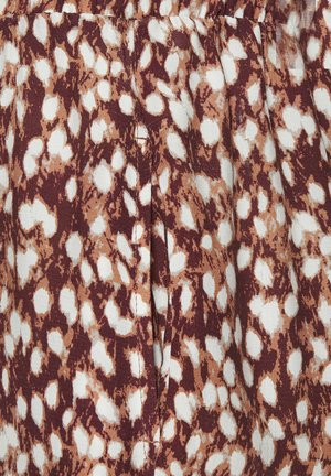 Braun-weißes tierisches Musterstoff mit Falten und sichtbaren vertikalen Nahtnähten.