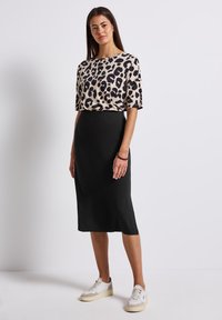T-Shirt mit Leopardenmuster in Beige und Schwarz, kombiniert mit einem einfarbigen schwarzen Midirock. Das Outfit wird durch weiße Sneakers abgerundet.