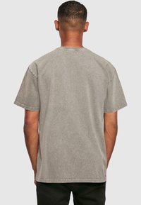 Gray short-sleeve t-shirt with a faded texture, crew neckline, and stitched hem, worn by a person from the back against a light background.