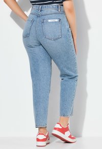 Helleblaue hochgeschnittene Jeans mit klassischem Fünf-Pocket-Design, ausgestattet mit einem fransigen Saum und strukturiertem Stoff, kombiniert mit rot-weißen Turnschuhen.