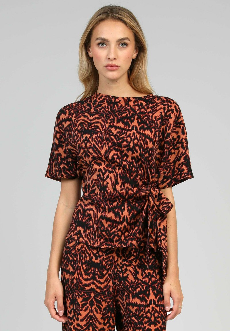 Haut à manches courtes en imprimé animal orange et noir, doté d'un lien à la taille et d'une coupe loose. Fabriqué à partir d'un tissu lisse et léger.
