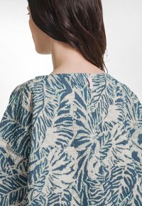 Struktureret stof i blå og creme med et bladmønster, med en bred halsudskæring og label på bagsiden.