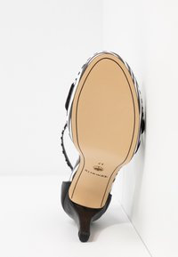 Vue de la semelle d'une chaussure à talon haut noire avec une semelle beige, indiquant la taille 37 et la marque "Tamaris."