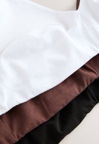 Gefaltete Baumwollstoffstücke in Weiß, Braun und Schwarz, in überlappenden Schichten auf einer hellen Oberfläche dargestellt.