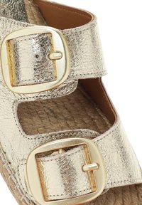 Gouden metallic sandalen met twee verstelbare gespen, voorzien van een gestructureerde bovenkant en een geweven jute zool. Dichtbijopname van het glanzende materiaal.