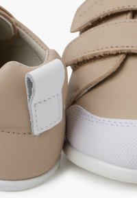 Scarpe sintetiche beige con doppie cinghie in velcro, tomaia testurizzata, suola in gomma bianca e un anello in tessuto bianco sul tallone per facilitare l'indossamento.
