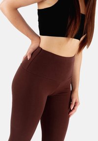 Brązowe legginsy wysokiego stanu z elastycznego materiału, o gładkiej fakturze i bocznymi kieszeniami dla wygody.