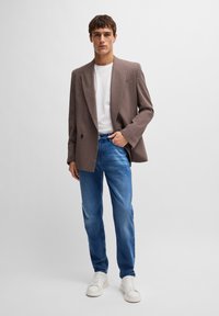 Rudas dvieilis švarkas dėvimas ant baltos marškinėlių, derinamas su mėlynais džinsais ir baltais sportbačiais. Švarkas pasižymi tekstūruota medžiaga ir ryškiais atlapais.