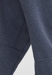 Pantalones deportivos de color azul oscuro hechos de una tela suave y texturizada; presentan costuras visibles y un ajuste ceñido en las piernas con un diseño entallado.