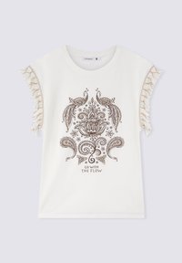 Maglietta bianca in cotone con un intricato motivo paisley e floreale marrone, con dettagli frangiati sulle maniche e la scritta "VAI CON IL FLUSSO."