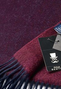 Wool blend scarf in dark red and navy with fringed edges. Includes a hang tag with a logo and product information. Soft texture.