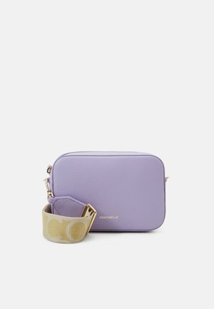 Sac bandoulière rectangulaire en cuir lavande avec fermeture éclair dorée et large sangle en tissu beige ornée de grandes lettres.