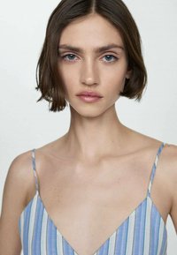 Light blue striped camisole with thin spaghetti straps, featuring a deep V neckline and a smooth, soft fabric against bare skin.