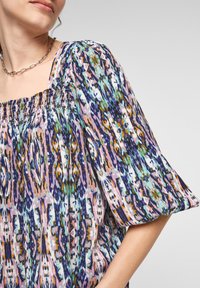 Mångfärgad blus med puffärmar, fyrkantig halsringning och samlade detaljer. Tyget har ett abstrakt mönster i nyanser av blått, rosa och grönt.
