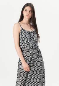 Abito a fantasia in bianco e nero con spalline sottili, vita cinchata e gonna fluente; presenta un motivo geometrico su tutta la superficie.