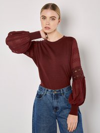 Bordowy sweter z przezroczystymi, bufkami, zdobiony teksturowanymi kropkami. Noszony z dżinsami w wysokim stanie w niebieskim kolorze, prezentującymi luźny krój.
