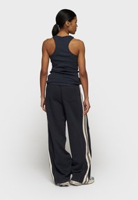 Navy Tanktop mit Racerback-Design, kombiniert mit lockeren schwarzen Hosen mit cremefarbenen Seitenstreifen, aus weichem Stoff.