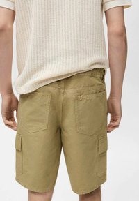 Pantaloni cargo in cotone khaki con vestibilità rilassata, caratterizzati da due tasche posteriori e tasche cargo laterali per maggiore utilità.