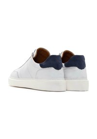 Baskets en cuir blanc avec un accent en suède gris au niveau du talon, semelle en caoutchouc plate et détail de fermeture éclair sur le côté. Texture lisse avec des coutures visibles.