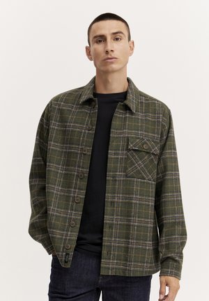 Groen geruite flanellen shirt met knopen, een borstzak, en contrasterende blauwe en witte lijnen, gecombineerd met een zwart t-shirt.