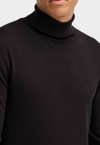 Maglione a collo alto nero realizzato in tessuto a maglia. Presenta un design aderente e una texture a coste nel colletto e all'orlo.