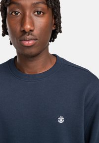 Felpa blu navy con colletto e polsini a coste, con un piccolo logo bianco sul lato sinistro del petto. Realizzata in tessuto morbido e texturizzato.