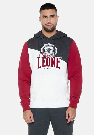 Homme portant un sweat à capuche tricolore avec des manches rouges, un corps blanc et une partie supérieure gris foncé, avec le texte et le logo "LEONE 1947" sur la poitrine.