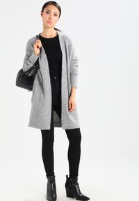 Gray knit cardigan with an open front, long sleeves, and a relaxed fit, paired with a black top, black skinny jeans, and black ankle boots.