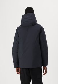 Mørkeblå polstret jakke med høj krave og oversized hætte, der har glat stof og minimalistisk design. Ingen synlig hardware eller logoer.