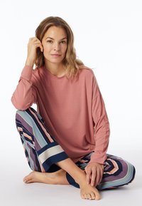 Růžový top s dlouhými rukávy v kombinaci s multibarevnými, pruhovanými kalhotami s širokými nohavicemi. Kalhoty mají různé pastelové barvy a námořnický akcent na lemu.