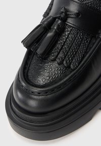 Černá kožená bota s texturovanými akcenty, detailními třásněmi a třásněmi. Silná černá podešev dodává stabilitu a kontrast elegantnímu designu.