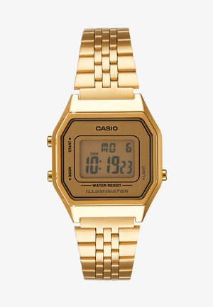 Montre numérique dorée avec un cadran rectangulaire, écran LCD, bracelet en acier inoxydable et boutons sur le côté. Présente un label résistant à l'eau.